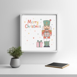 May include: A white framed print with a colorful "Merry Christmas" greeting and a cartoon illustration of a nutcracker holding a gift. The background is decorated with small pink hearts.