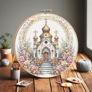 May include: A round embroidery hoop with a cross-stitch design of a white church with gold accents surrounded by pink and yellow flowers.