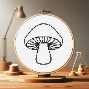 May include: Black and white cross-stitch embroidery of a mushroom in a round wooden embroidery hoop.