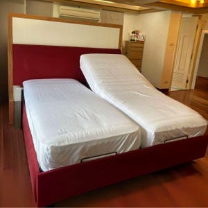 Puede incluir: Una cama roja ajustable con una cabecera blanca y dos colchones separados cubiertos con sábanas blancas. El marco de la cama es de color rojo intenso y la cabecera tiene un marco de madera.