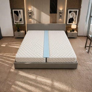 May include: A light blue bed bridge connector placed between two white quilted mattresses on a gray upholstered bed frame. The mattresses feature a diamond-stitched pattern and are positioned side-by-side within a bedroom setting.