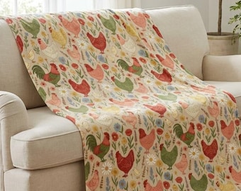 May include: A patterned throw blanket with a chicken design draped over a beige sofa. The blanket's pattern includes red, green, and pink chickens with floral accents. The room has a warm, inviting atmosphere.