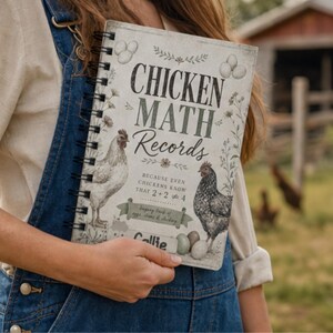 Könnte beinhalten: Ein spiralgebundenes Notizbuch mit dem Titel "CHICKEN MATH RECORDS" und Illustrationen von Hühnern und Eiern. Auf dem Cover steht der Text "BECAUSE EVEN CHICKENS KNOW THAT 2+2=4". Das Notizbuch wird von einer Person in einer Jeanslatzhose gehalten.