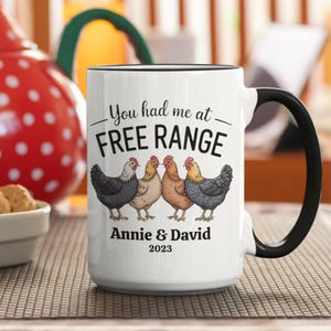 May include: White ceramic mug with a black handle and rim, featuring the text "You had me at FREE RANGE" and four illustrated chickens. The mug is personalized with "Annie & David 2023".