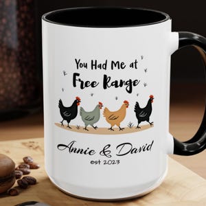 Può includere: Tazza in ceramica bianca con interno e manico neri. La tazza presenta il testo "You Had Me at Free Range" sopra una fila di quattro polli dei cartoni animati. Sotto, il testo "Annie & David est 2023".