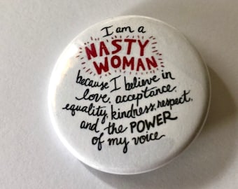 Puede incluir: Botón blanco con texto negro y rojo que dice "Soy una NASTY WOMAN porque creo en el amor, la aceptación, la igualdad, la amabilidad, el respeto y el PODER de mi voz."