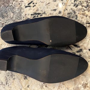 K&ouml;nnte beinhalten: Ein Paar marineblaue Schuhe mit Absatz und dunklen Sohlen. Die Schuhe haben eine abgerundete Spitze und einen kleinen Absatz. Die Sohlen sind mit horizontalen Linien f&uuml;r den Halt strukturiert. Die Schuhe sind wahrscheinlich aus Wildleder oder einem &auml;hnlichen Material.