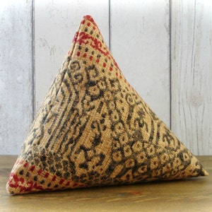 May include: A triangular pillow with a patterned fabric cover. The fabric is a beige color with black and red geometric designs.