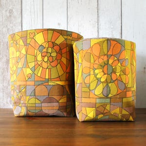 May include: Two cylindrical storage baskets with a geometric pattern in shades of yellow, orange, brown, and green. The pattern features circles, squares, and abstract shapes.