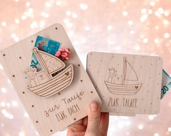 May include: Two wooden cards with a sailboat design and the text "zur Taufe für dich" and "zur Taufe". The cards have a slot for money or a gift card.