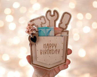 Pode incluir: Um cartão de madeira com um bolso e um design de ferramentas. O cartão diz "Feliz aniversário" e tem um pequeno coração e flores anexadas.