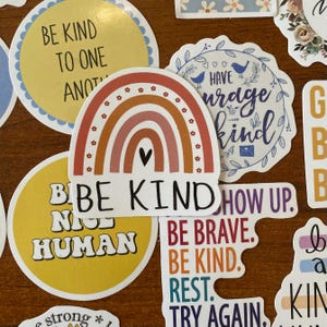 May include: Assortment of colorful stickers with positive messages, including "Be Kind", "Be Brave", "Rest", "Try Again", "Have Courage Be Kind", "Be Nice Human", and "Show Up".