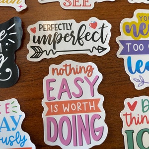 May include: A set of colorful stickers with motivational quotes. The stickers feature phrases like "Perfectly Imperfect", "Nothing Easy Is Worth Doing", and "You Never Learn Too Late".