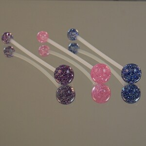 May include: Four pairs of body jewelry with clear plastic bars and colorful glitter balls. Two pairs have pink glitter balls and two pairs have blue glitter balls.