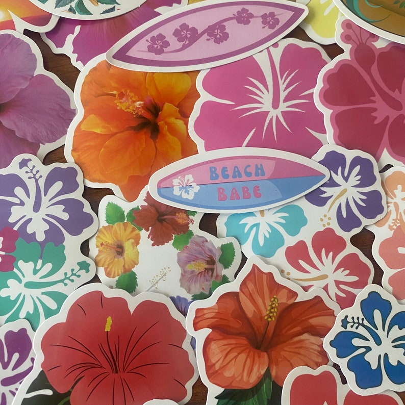 May include: A collection of colorful stickers featuring hibiscus flowers and surfboard designs. The stickers are in various shades of pink, orange, red, purple, and blue. One sticker reads "Beach Babe".