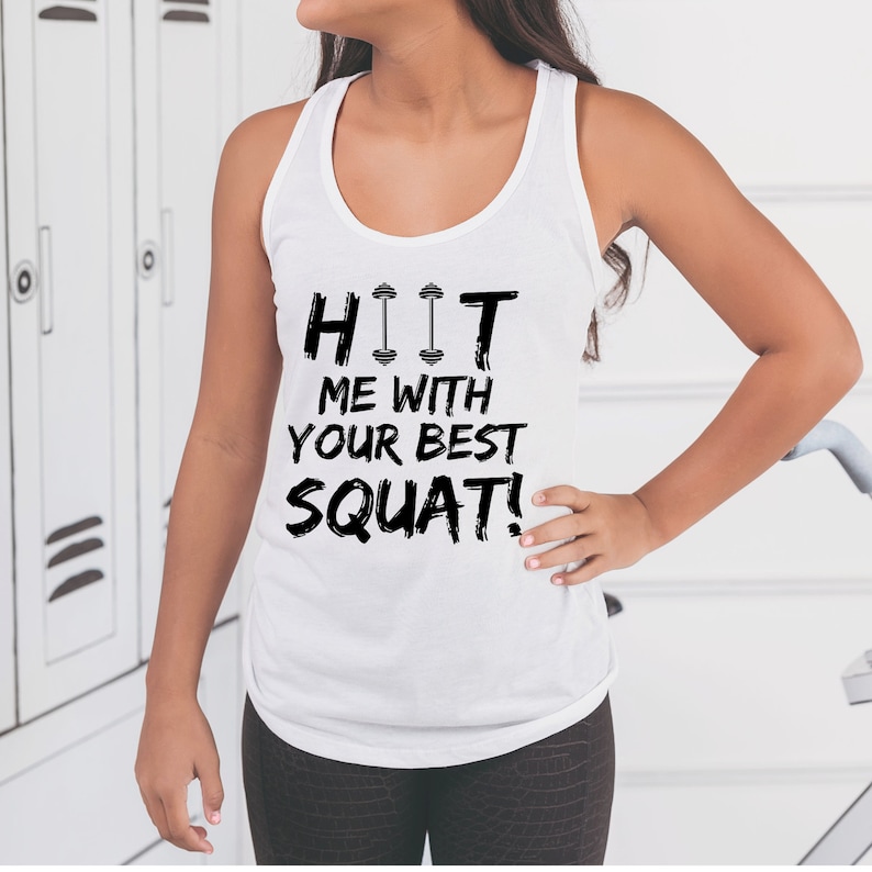 May include: White tank top with black text that reads "HIT ME WITH YOUR BEST SQUAT!" with a dumbbell graphic above the word "HIT".