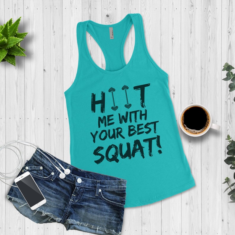 May include: A turquoise tank top with a black graphic that says "HIIT ME WITH YOUR BEST SQUAT!" The graphic includes two black dumbbells.