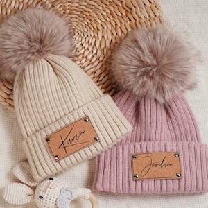 Può includere: Due berretti invernali in maglia con pon pon in pelliccia sintetica. I berretti hanno toppe in pelle personalizzate con i nomi "Karen" e "Jordan" scritti in corsivo.