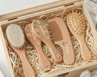 May include: A wooden keepsake box with the text Baby's First Keepsake on the lid, containing four wooden hair brushes and a comb. Each item features a floral rose pattern and the name Amelia printed on the handle, resting on wood shavings.