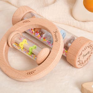 以下が含まれることがあります： カラフルなビーズと小さな動物のフィギュアが入った透明なチューブが付いた、2つの木製のベビーラトル。1つは丸く、もう1つは円筒形です。「Francis」という名前が両方のラトルに刻まれています。