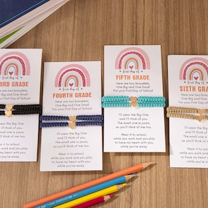 Puede incluir: Cuatro tarjetas con dise&ntilde;os de arco&iacute;ris y las palabras "primer d&iacute;a de" seguidas de "Tercer Grado", "Cuarto Grado", "Quinto Grado" y "Sexto Grado". Cada tarjeta tiene un par de pulseras con un dije de coraz&oacute;n y un mensaje sobre usar las pulseras en la escuela.