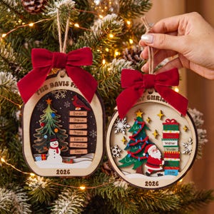 May include: Two wooden Christmas ornaments with red velvet bows and twine hangers. The left ornament features a snowman, a tree, a cardinal, and the text THE DAVIS FAMILY and 2026. The right ornament shows Santa, a tree, and the text MERRY CHRISTMAS and 2026.
