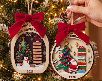 May include: Two wooden Christmas ornaments with red velvet bows and twine hangers. The left ornament features a snowman, a tree, a cardinal, and the text THE DAVIS FAMILY and 2026. The right ornament shows Santa, a tree, and the text MERRY CHRISTMAS and 2026.