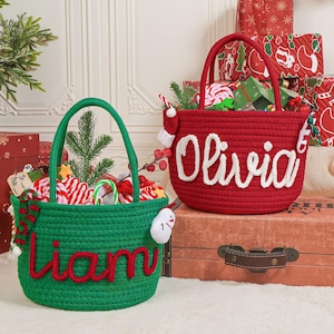 Könnte beinhalten: Zwei Weihnachts-Seilkörbe, einer grün und einer rot, gefüllt mit festlichen Leckereien. Der rote Korb trägt den Namen "Olivia" in Weiß, der grüne Korb "Liam" in Rot. Festliche Geschenke und Dekorationen umgeben die Körbe.