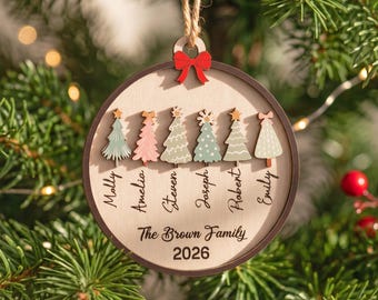 May include: A round wooden Christmas ornament featuring six stylized trees in various colors and patterns. Below each tree is a name: Molly, Amelia, Steven, Joseph, Robert, and Emily. The text The Brown Family 2026 is printed below.