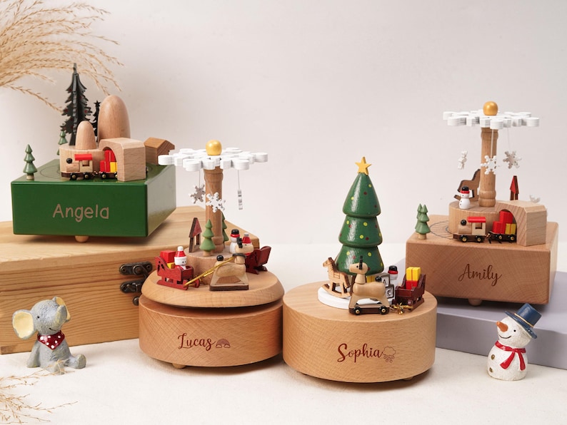 May include: Four wooden music boxes featuring festive holiday themes. One green box is engraved with Angela, two round light wood boxes are engraved with Lucas and Sophia, and one square light wood box is engraved with Amily. Includes small figurines.
