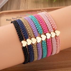 Puede incluir: Un conjunto de diez pulseras trenzadas de colores con dijes de coraz&oacute;n de oro. Las pulseras son de color negro, azul marino, caqui, morado, azul, turquesa, rosa intenso, rosa, melocot&oacute;n y lavanda.