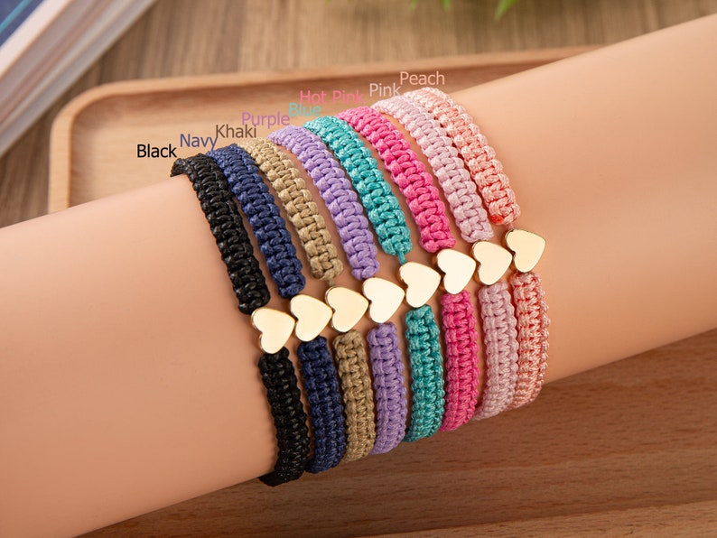 Puede incluir: Un conjunto de diez pulseras trenzadas de colores con dijes de coraz&oacute;n de oro. Las pulseras son de color negro, azul marino, caqui, morado, azul, turquesa, rosa intenso, rosa, melocot&oacute;n y lavanda.