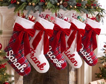 May include: Five Christmas stockings hanging in a row, each featuring a red and green plaid pattern, a white cuff, and a large red velvet bow. The stockings are personalized with the embroidered names Sarah, Frank, Nicole, Aiden, and Dustin.