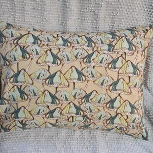May include: Rectangular pillow with a repeating pattern of stylized mushrooms. The mushrooms have cream-colored caps with teal and yellow accents, set against a light tan background. The pillow is likely made of fabric and is designed for decorative use.