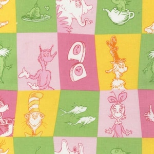 May include: Fabric with a repeating pattern of whimsical cartoon characters in pink, green, and yellow squares. The illustrations include a pink creature, a character with a tall hat, and other playful designs. The fabric is likely cotton or a similar material.