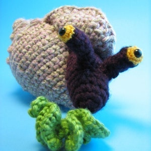 May include: A crocheted purple and pink snail with yellow eyes and a green crocheted seaweed accessory.