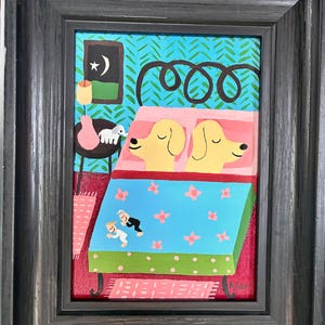 Puede incluir: Obra de arte enmarcada que representa a dos perros amarillos durmiendo en una cama con una manta azul con estampado floral. El fondo presenta una pared turquesa con un patrón verde. Una pequeña mesa sostiene un jarrón y una vela.