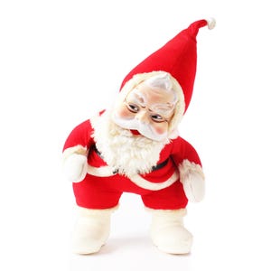 May include: A vintage Santa Claus doll in a red suit and hat, with a white beard and trim. The doll is in a bent posture with a smiling face. A festive Christmas decoration.