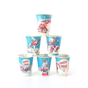 May include: A stack of six vintage paper cups with a winter theme. The cups are light blue with illustrations of a woman in a red winter outfit ice skating and the words "Frosty Treat".