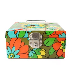 May include: A vintage metal storage box with a colorful floral pattern in orange, yellow, blue, and green on an olive green background. The box has a silver handle and a latch closure.