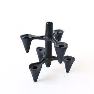 May include: A black metal candle holder with a unique, multi-armed design. The holder features a central column with six candle holders, each with a conical shape. The overall height is approximately 6 inches.
