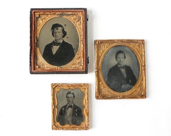 May include: Three antique portrait photographs in ornate gold frames. The portraits feature men in dark suits and bow ties. The frames have intricate detailing and are in varying sizes, with one rectangular and two oval-shaped.