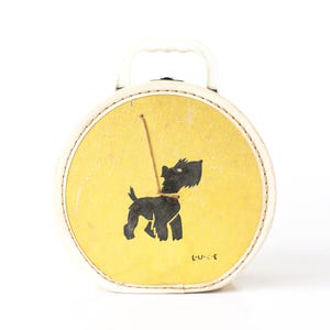 May include: A vintage, round, white and yellow suitcase with a black dog silhouette on the front. The suitcase has a white handle and a textured yellow background. The dog is on a leash. The text "L.U.C.E" is on the bottom right.