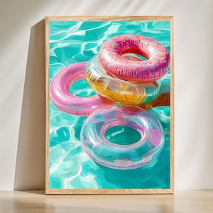Puede incluir: Impresión enmarcada que presenta varios flotadores inflables para piscina. Los flotadores son en tonos de rosa, amarillo y transparente, con un flotador en forma de rosquilla rosa glaseada en la parte superior. El agua es de color turquesa brillante, creando una escena veraniega.