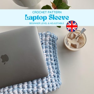 Puede incluir: Una funda para portátil de crochet en azul y blanco, con un portátil apoyado encima. La funda está hecha con un patrón de punto sencillo y es ajustable para adaptarse a diferentes tamaños de portátiles. La imagen también incluye una taza de café helado y una pequeña planta en maceta.
