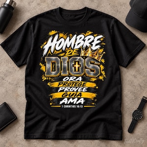 Könnte beinhalten: Ein schwarzes T-Shirt mit einem Grafikdesign, das den Text "HOMBRE DE DIOS" in Weiß und Metallic-Grau, eine goldene Krone und ein Kreuz zeigt. Darunter stehen die Wörter "ORA PROTEGE PROVEE GUÍA AMA" in Weiß auf gelben Pinselstrichen, mit "1 CORINTIOS 16:13" am unteren Rand.