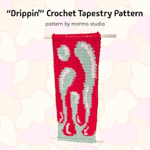 Puede incluir: Un tapiz de pared de crochet con un diseño "Drippin'" en rojo, verde y rosa. El tapiz está colgado de una varilla de madera.