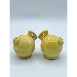 Puede incluir: Dos saleros y pimenteros de cerámica amarilla. Cada salero y pimentero tiene la forma de un pequeño pájaro con un cuerpo redondeado, un pequeño pico y un ala decorativa. Los saleros y pimenteros tienen un acabado brillante.