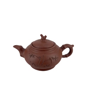 以下が含まれることがあります： 蓋と曲がった取っ手が付いた茶色のセラミックティーポット。 ティーポットは注ぎ口があり、エッチングされた竹と植物のデザインで装飾されています。 蓋には小さな枝のような取っ手が付いています。