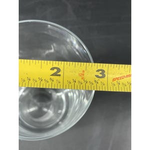 May include: A clear glass with a yellow measuring tape across the top. The tape reads 5 cm to 7.6 cm. The glass is on a dark surface.